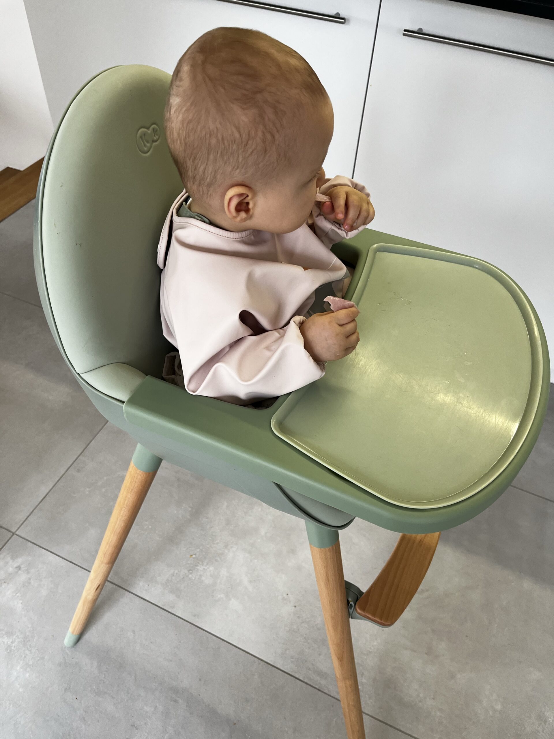 Patachou dans sa chaise haute verte, avec son bavoir rose.