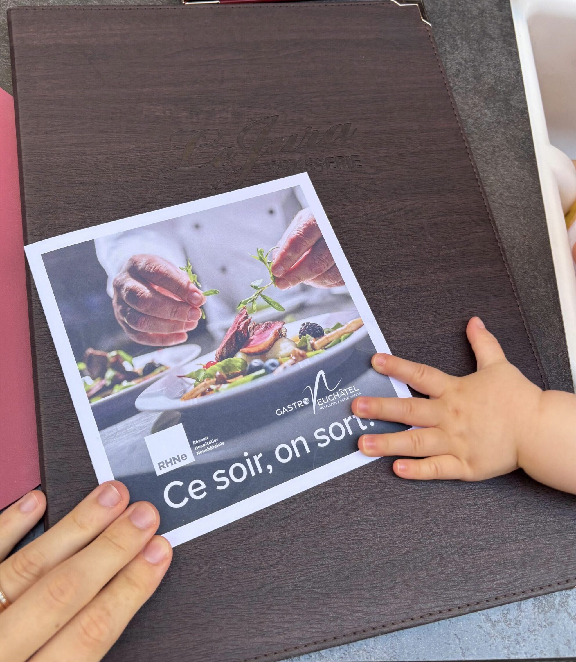 Le bon reçu à la maternité, posé sur la carte de la brasserie Le Jura, entre nos mains et celles de bébé.