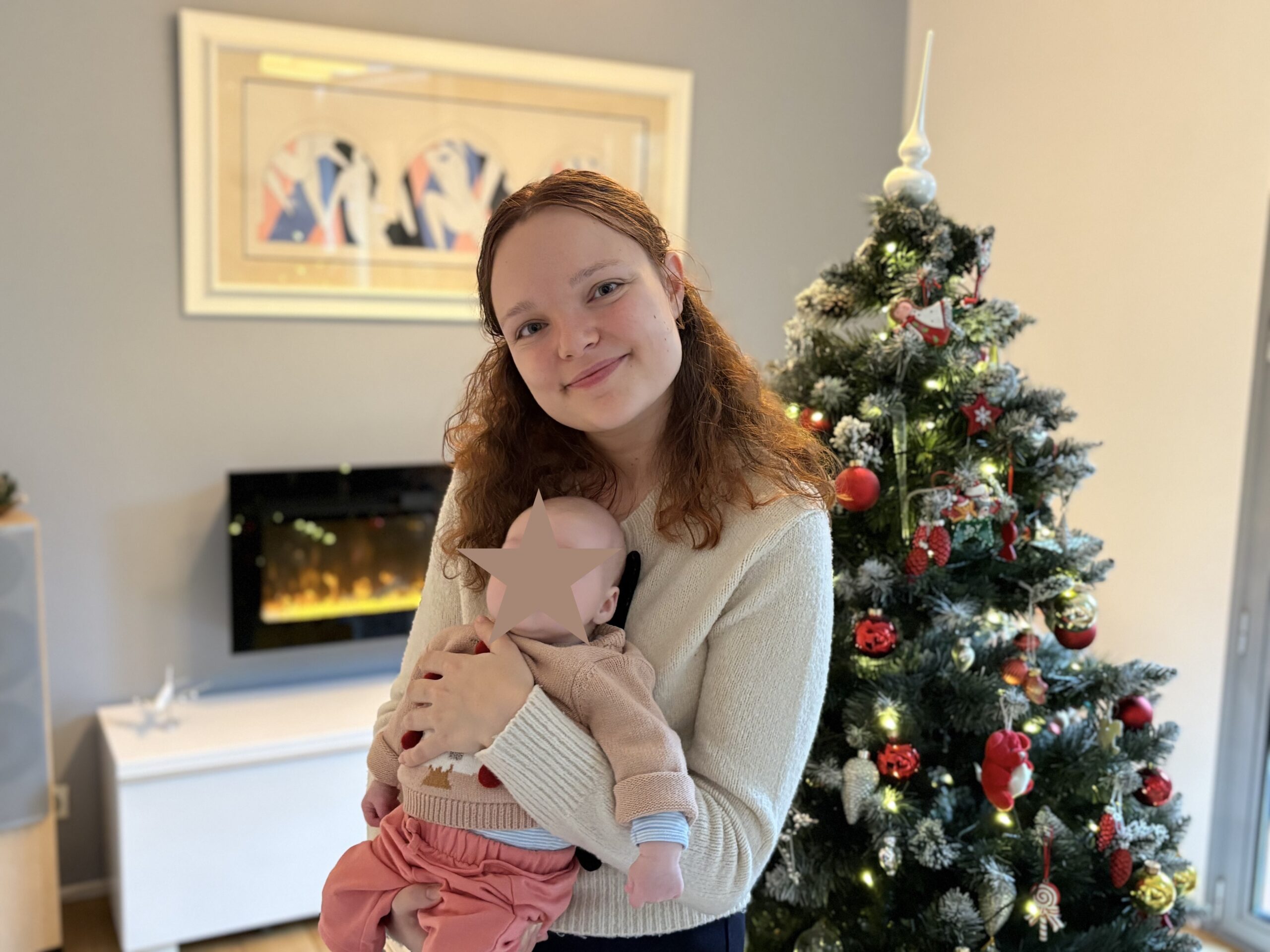 Mamanboussole tenant son bébé près d’un sapin de Noël.
